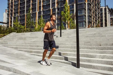 Young man exercising outside. Guy jogging or slow running besides steps Stock Photos