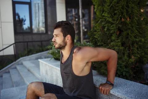 Young man exercising outside. Guy doing reverse push ups holding hands behind Stock Photos