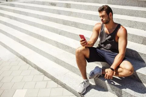Young man exercising outside. Guy sit and rest on steps after hard workout. Hold Stock Photos