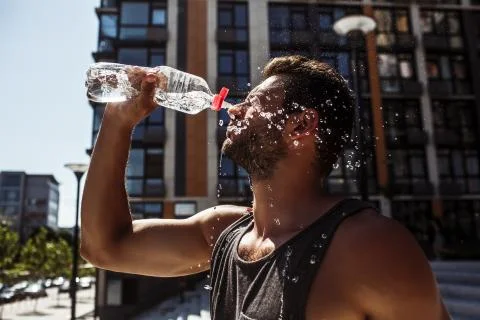 Young man exercising outside. Guy pouring some fresh water out of bottle on his Stock Photos
