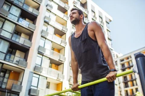 Young man exercising outside. Low view of strong guy holding his upper body Stock Photos