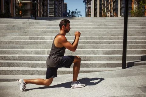Young man exercising outside. Side view of guy athletist sitting in one leg Stock Photos