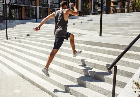 Young man exercising outside. Side back view of strong fast guy jumping up Stock Photos