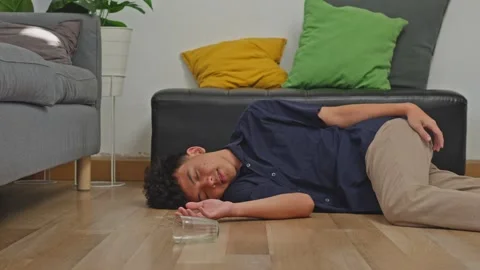 Young man experience vertigo slips and falls flat onto living room floor Stock Footage 335886078