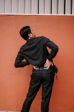 Young man experiencing lower back pain against orange wall Stock Photos