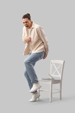 Young man experiencing sharp pain in buttocks after sitting on broken chair,  Stock Photos