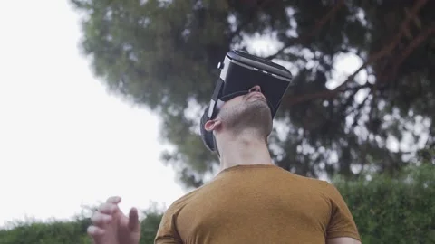 Young man experiencing virtual reality wearing VR gaming headset outdoors Stock Footage 133374152