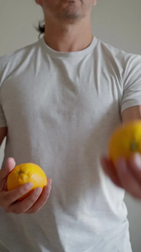 A young man expertly juggles oranges in a minimalist setting, balancing motion Stock Footage 311052106