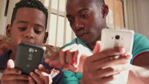 Young Man Explaining Mobile Phone Internet To Boy At Home Stock Footage