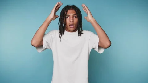 Young man expresses frustration with hands raised against a blue background.. Stock Footage 313273980