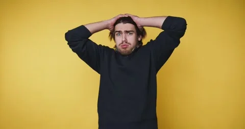 Young man expresses frustration by holding his head, capturing a relatable .. Stock Footage 314336955
