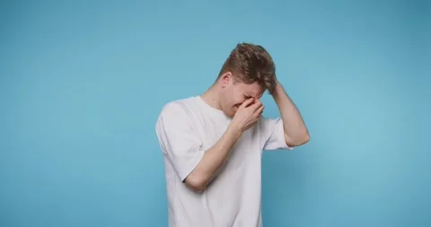Young man expresses his frustration while holding his head, against vibrant.. Stock Footage 313279971