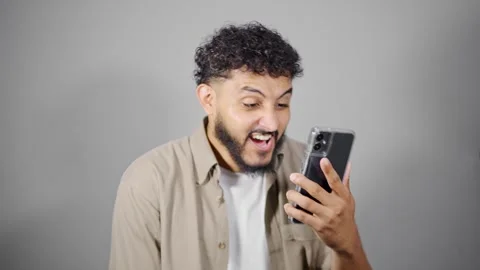 Young man expressing various emotions while looking at his smartphone Stock Footage 314785466