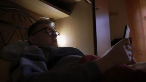 Young man in eyeglasses lying down on the couch at home in the evening, using Stock-Footage 143724099