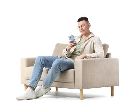 Young man in eyeglasses using mobile phone on grey sofa against white backgro Stock Photos