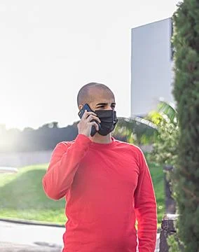 Young man with face mask checking his mobile phone and speaking in the park Stock Photos