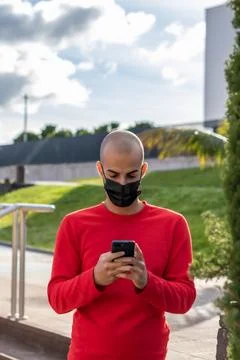 Young man with face mask checking his mobile phone and speaking in the park Stock Photos