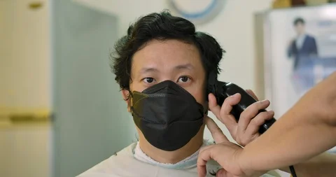 Young man in face mask looking at camera while getting haircut. Video stock 129057101