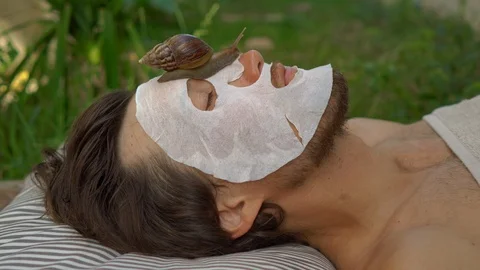 Young man with a face mask with snail mucus. Snail crawling on a face mask. SPA Stock Footage 117554229
