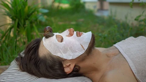 Young man with a face mask with snail mucus. Snail crawling on a face mask. SPA Stock Footage 117556899