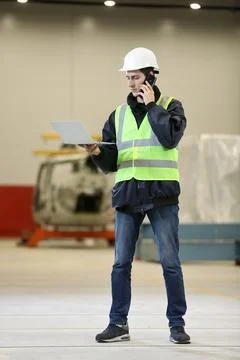 Young man, factory engineer in a work dress and white hard hat holding smartp Stock Photos