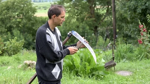 Young man farmer sharpening sickle scythe with stone in summer Stock Footage 97682065