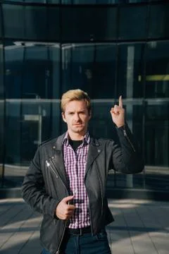 A young man in fashionable clothes points his finger up at the copy space. The Stock Photos