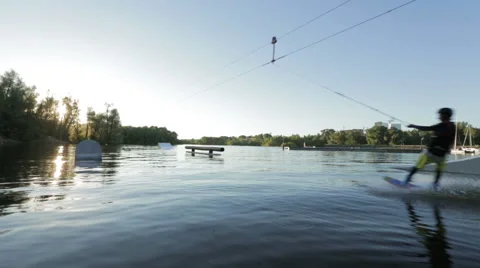 The young man fast rides on a wakeboard against the sunset in the wake park Stock Footage 56196003