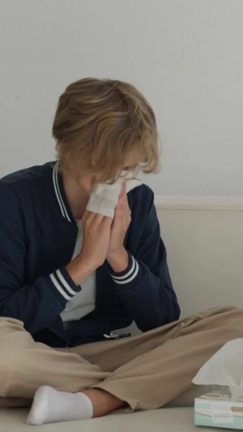 Young man feeling unwell on a couch with runny nose and tissues, sneezing Stock Footage 319915944