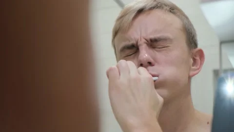A young man feels pain while brushing his teeth with a toothbrush, close-up Stock Footage 230444348