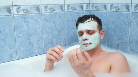 Young man is filing his nails sitting in bathroom with mask on face. Video stock 153577935