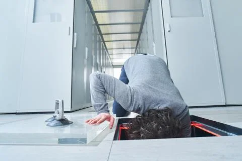 Young man fixing something in the floor hatch. Data center. Servers Stock Photos