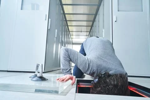 Young man fixing something in the floor hatch. Data center. Servers Stock Photos