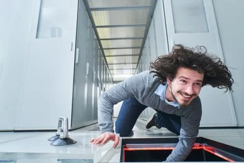 Young man fixing something in the floor hatch. Data center. Servers Stock Photos