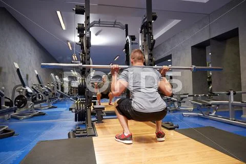 Young man flexing muscles with bar in gym Stock Photos