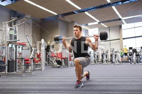 Young man flexing muscles with barbell in gym Stock Photos
