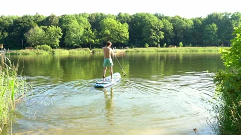 Young man floating down a river standing on a supboard Stock Footage 246798948