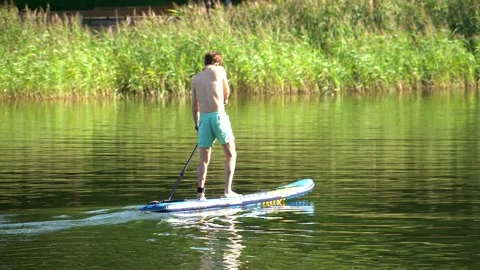 Young man floating down a river standing on a supboard Stock Footage 247034755