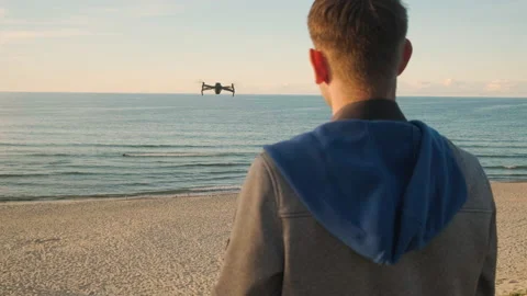 A young man flying quadcopter drone out over the sea at sunset Stock Footage 219919022