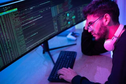 Young man focused on coding in a dimly lit room with large monitors display.. Stock Photos