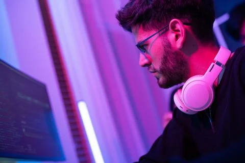 Young man focused on coding in a vibrant, modern workspace illuminated by c.. Stock-Fotos