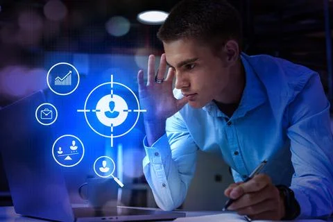 Young man focused on digital interface while working on laptop in modern office Stock Photos