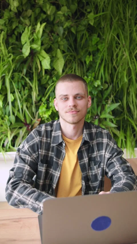 A young man is focused on his laptop while sitting at a wooden table in a bright Stock Footage 346151486