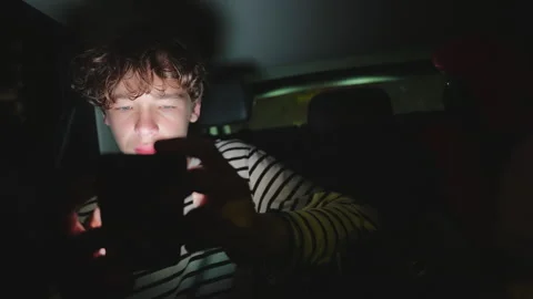 Young Man Focused on Phone Screen in Dark Car at Night Stock Footage 335394228