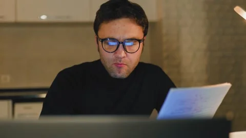 Young man focused on reading documents at home late at night Видео 305151832