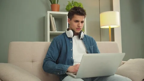 Young man focused on solving a problem while working on a laptop with headphones Stock Footage 297923180