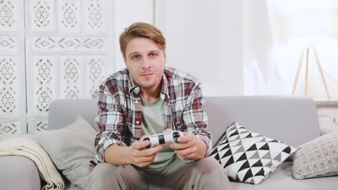 Young man focused on video game while sitting on a comfortable couch in a cozy Stock Footage 320440259