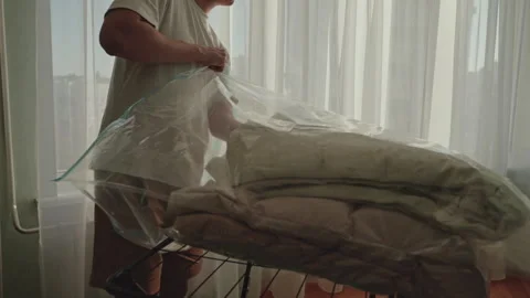 Young man folding plush blanket, sliding into transparent vacuum storage bag Stock Footage 304862155