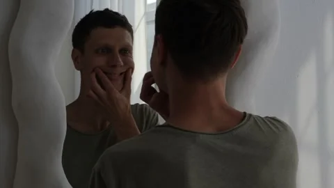 Young man forcing a smile in the mirror. Concept of depression, mental health Video stock 311762966