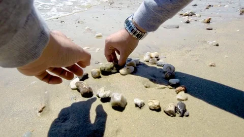 Young man forms a heart with small stones on a beach by the sea Stock Footage 113462411